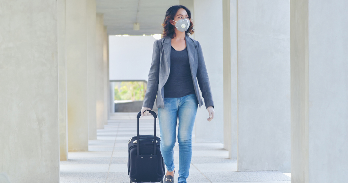 Woman in airport with luggage and mask post-COVID